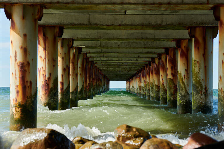 Corrosion showing on pillars supporting a bridge along a saltwater, oceanic coastline