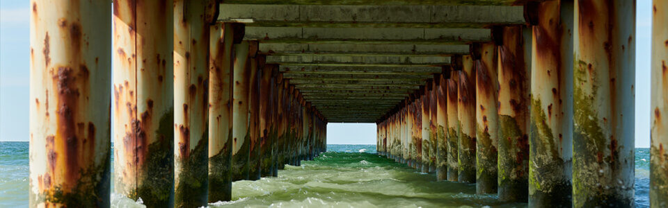 Corrosion showing on pillars supporting a bridge along a saltwater, oceanic coastline